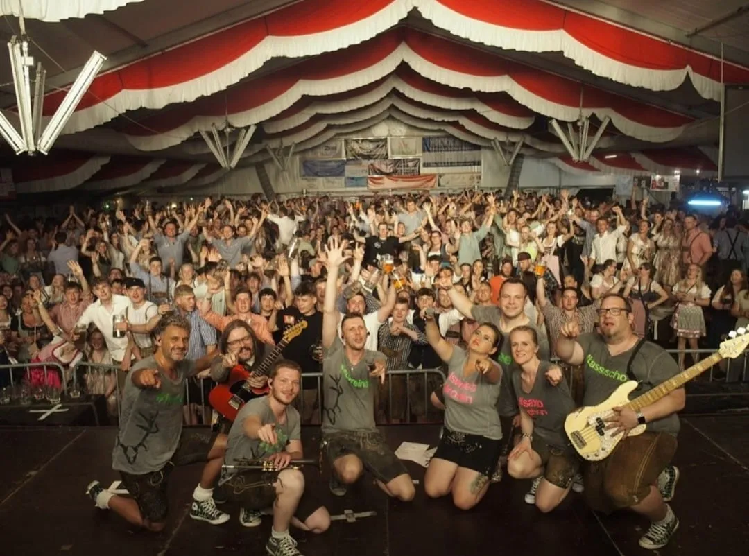 Die Band Albkracher posiert auf der Bühne vor dem voll besetzten, rot-weiß geschmückten Festzelt, das Publikum jubelt mit erhobenen Armen