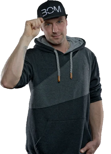 DJ DenniS in Kapuzenpullover und schwarzer Basecap tippt grüßend an den Schirm seiner Kappe