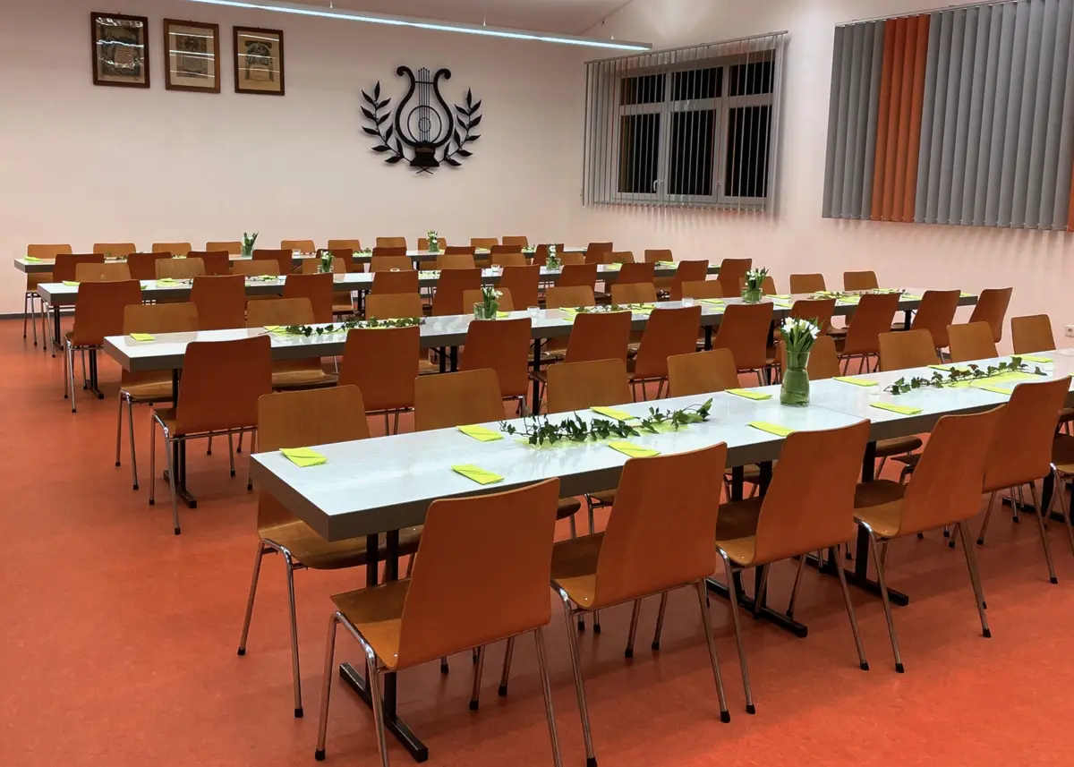 Der helle Saal des Musikerheims mit gedeckten Tischreihen und Blumenschmuck