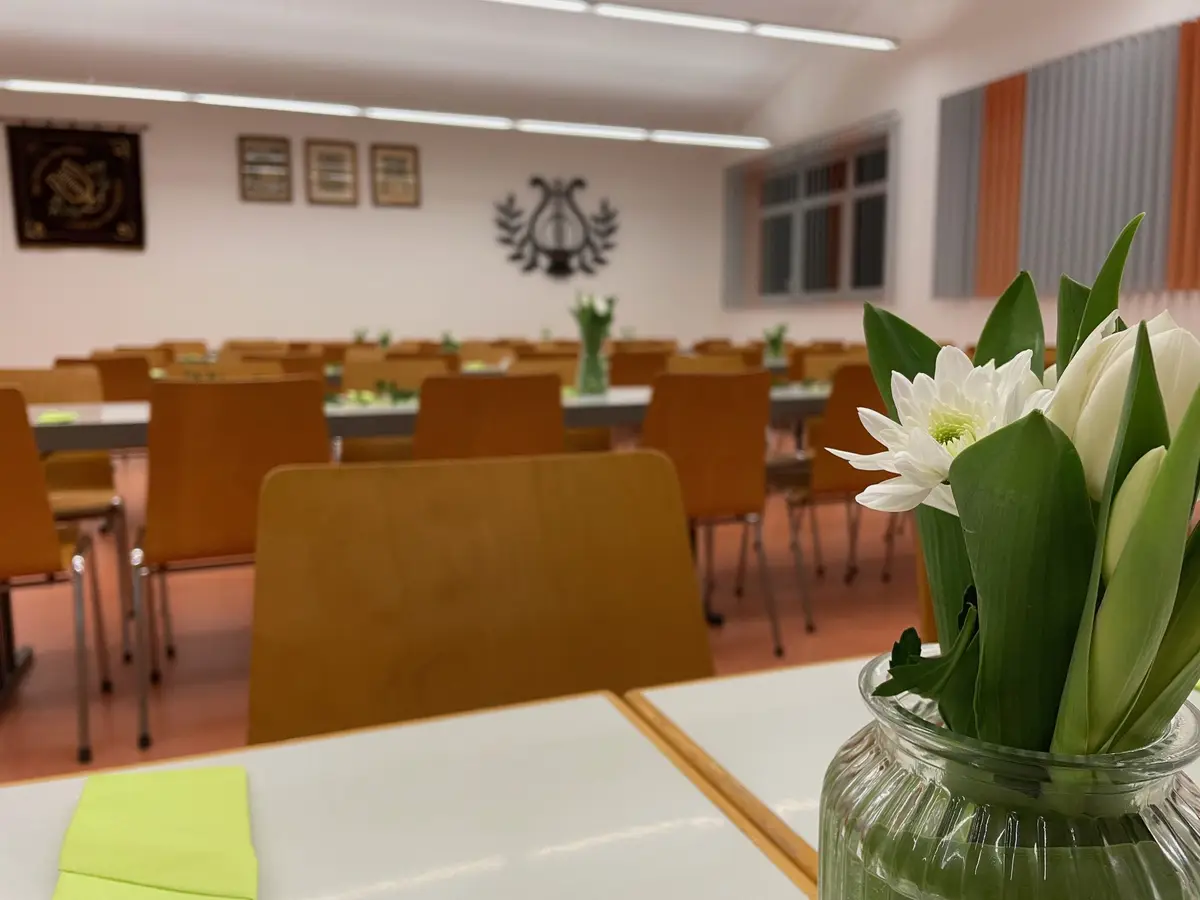 Ein Blumenstrauß aus weißen Tulpen auf einem gedeckten Tisch, dahinter der Saal