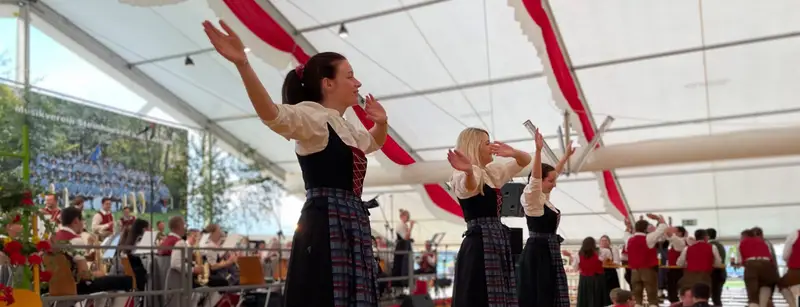 Sängerinnen in Tracht tanzen auf der Bühne im vollen Festzelt